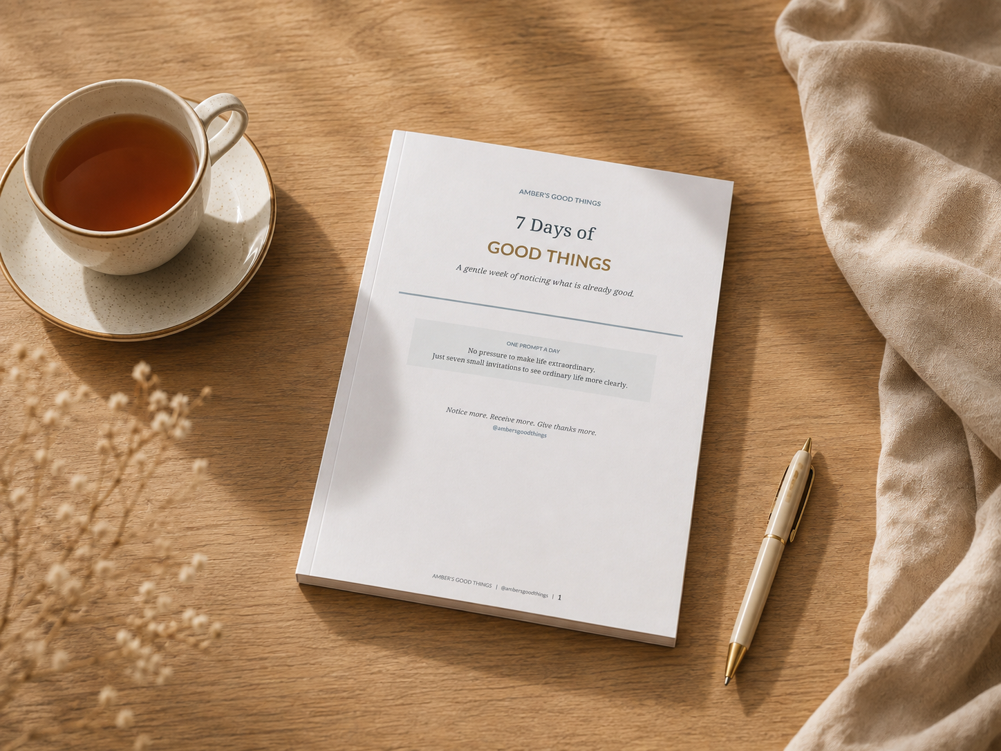 Printed 7 Days of Good Things workbook on a warm wooden desk beside a cup of tea and pen.